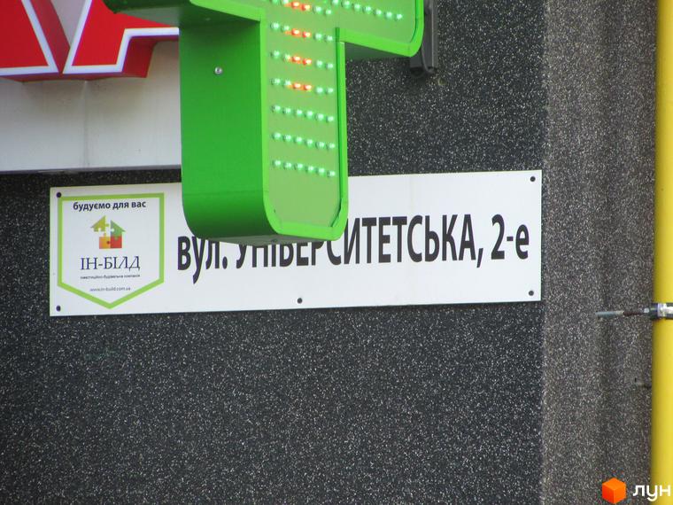 Фасад будинку з вивіскою: вулиця Університетська, 2-е. Поруч реклама будівельної компанії