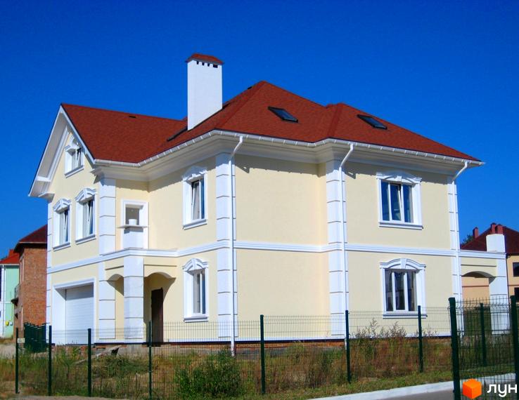 Двоповерховий будинок з червоним дахом та світлими стінами. На передньому плані зелений паркан та рослинність.