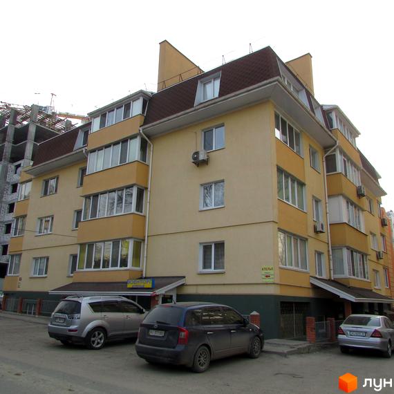 Зовнішній вигляд будинку на вулиці Українська, 85. Багатоповерхова будівля з коричневим дахом та припаркованими автомобілями.