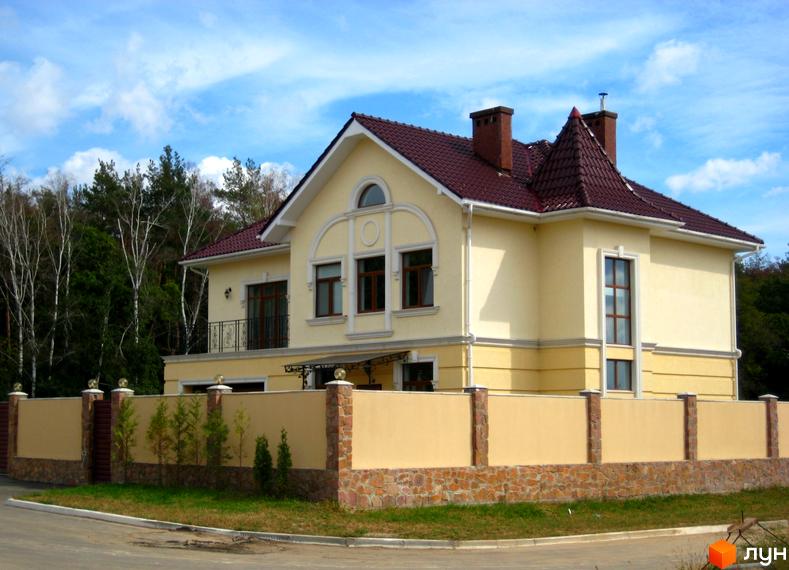 Двоповерховий будинок з червоною черепицею та світлими стінами. На передньому плані паркан з декоративним каменем та зелені насадження.