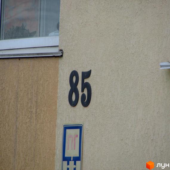 Фасад будинку за адресою вулиця Українська, 85. На стіні номер будинку та знак зупинки громадського транспорту.