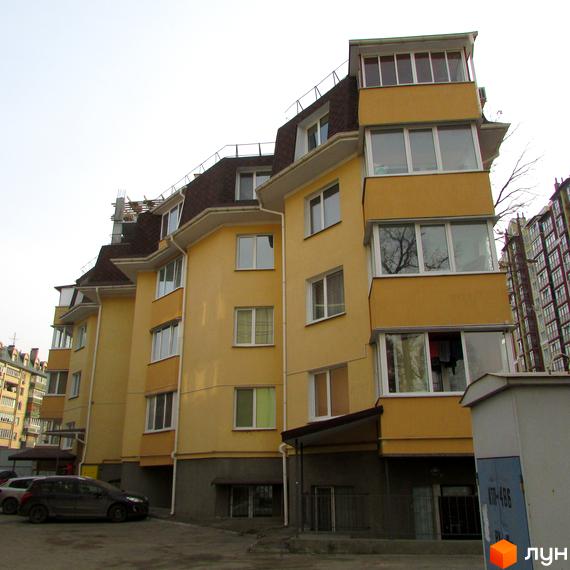 Зображення фасаду будинку на вулиці Українська, 85. Багатоповерхова будівля з жовтим фасадом та коричневим дахом, поруч припарковані автомобілі.