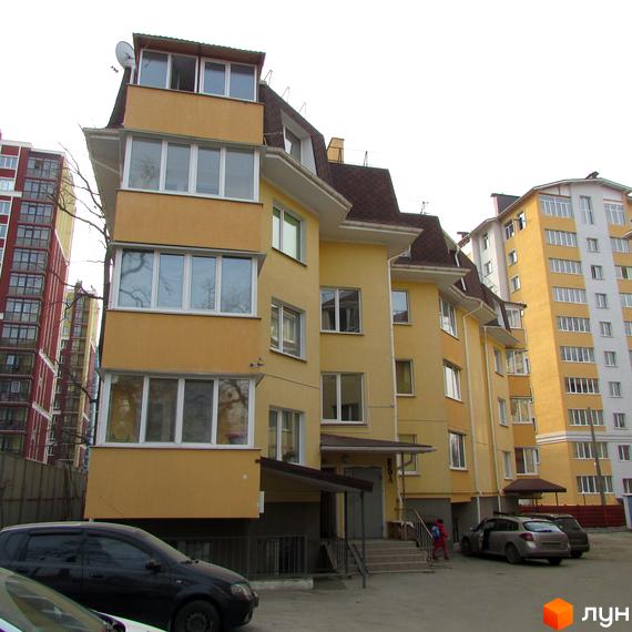 Зображення фасаду будинку по вулиці Українська, 85. На передньому плані автомобілі та прибудинкова територія.