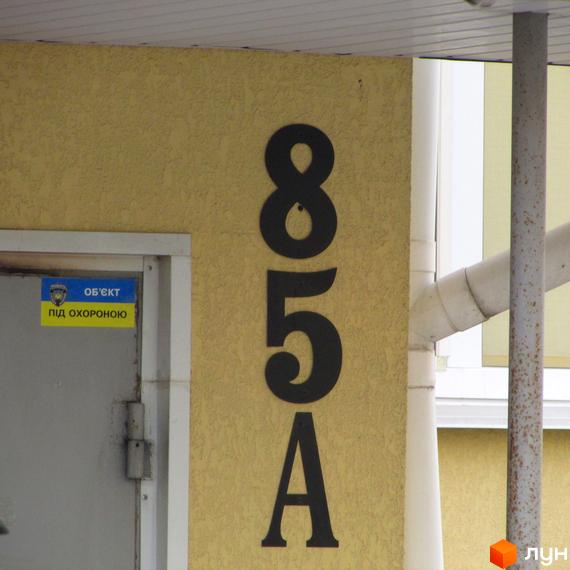 Фото будинку за адресою вул. Українська, 85А. На жовтій стіні великі чорні цифри 85А, поруч двері з табличкою 'Об'єкт під охороною'.