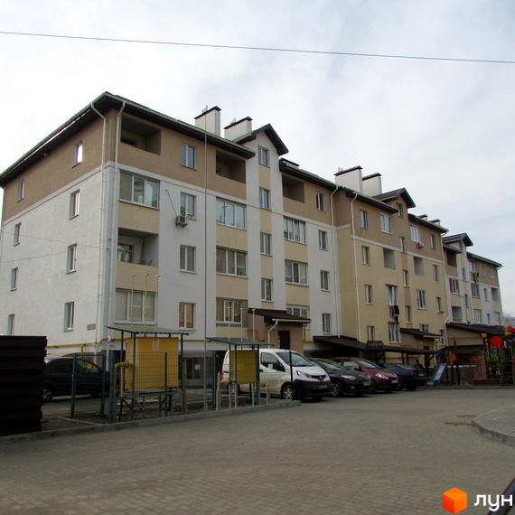Зовнішній вигляд будинку по вулиці Новооскольська, 8в. На передньому плані прибудинкова територія з парковкою та дитячим майданчиком.