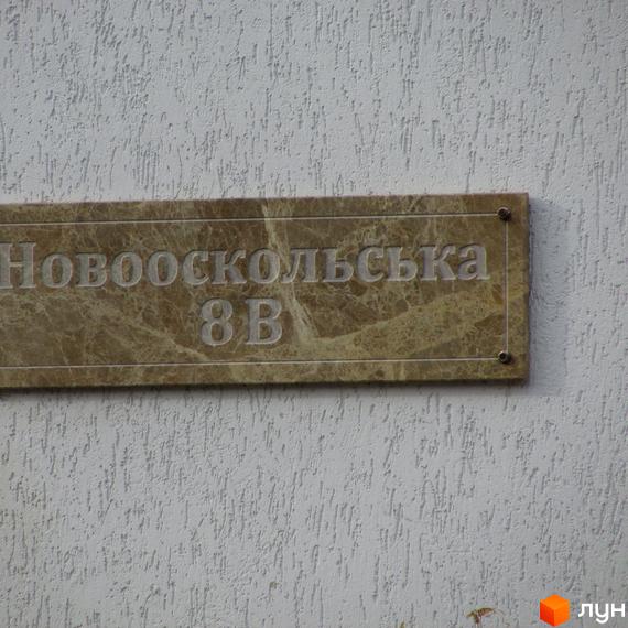 Фото таблички з адресою будинку: вулиця Новооскольська, 8В. Фасад будинку з текстурною штукатуркою.