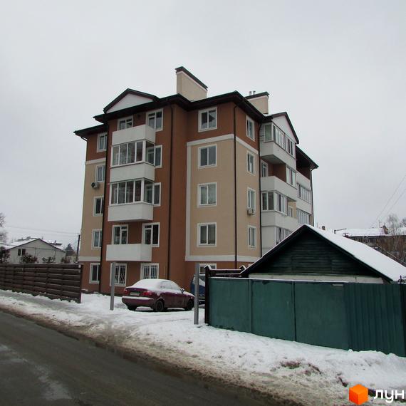 Житловий комплекс Ирпенский дворик: багатоповерховий будинок з коричнево-бежевим фасадом та білими балконами. Навколо сніг та припаркований автомобіль.