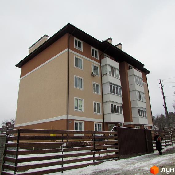 Житловий комплекс Ирпенский дворик: багатоповерховий будинок з бежево-коричневим фасадом та білими балконами. На передньому плані засніжений дерев'яний паркан.