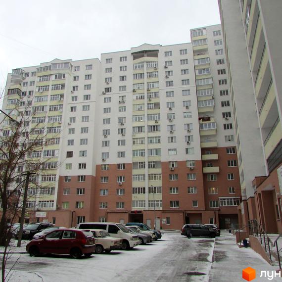 Житловий комплекс Княжа гора: багатоповерховий будинок з білим та коричневим фасадом, поруч засніжена парковка з автомобілями.