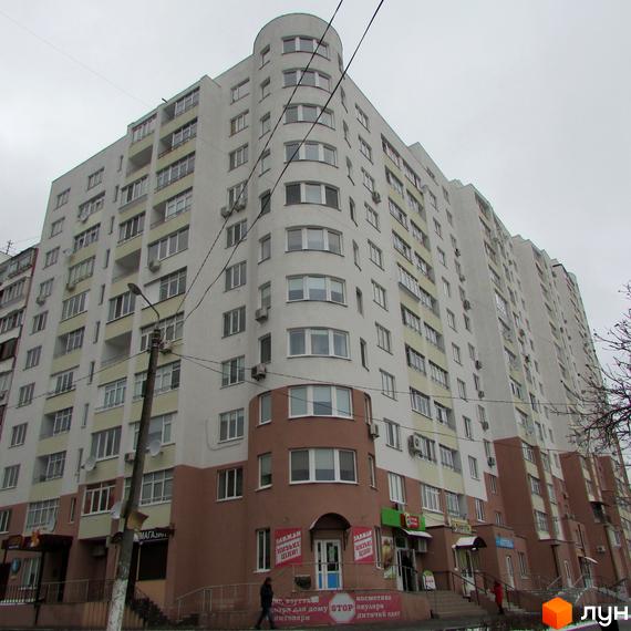 Житловий комплекс Княжа гора: багатоповерховий будинок з білим фасадом, коричневими елементами та заокругленим кутом. На перших поверхах розташовані магазини.