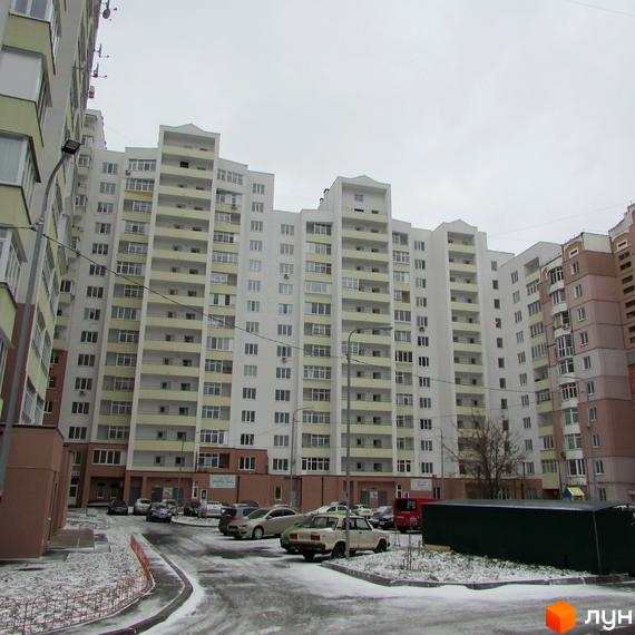 Житловий комплекс Княжа гора: багатоповерховий будинок білого кольору з жовтими балконами та засніженим двором з автомобілями.