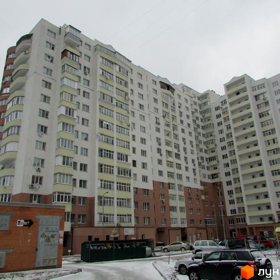 Житловий комплекс Княжа гора: багатоповерховий будинок з білим фасадом та світлими балконами. Прибудинкова територія вкрита снігом, видно автомобілі.