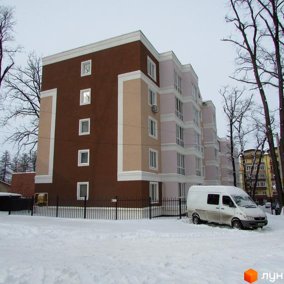Житловий комплекс Фортуна з багатосекційним фасадом коричневого та світло-рожевого кольорів, прикрашений білими архітектурними елементами. Навколо засніжена територія з огорожею та деревами.