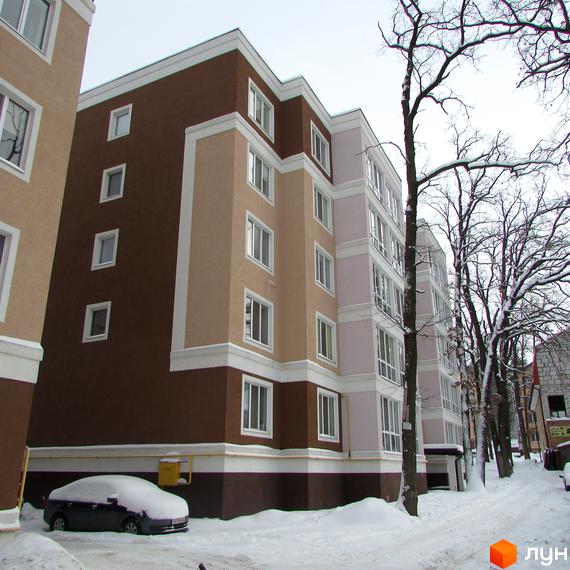 Житловий комплекс Фортуна взимку. Багатоповерховий будинок з коричнево-бежевим фасадом та білими елементами, засніжена прибудинкова територія.