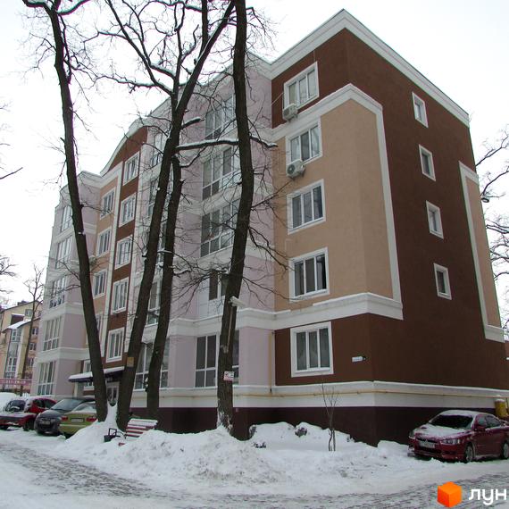 Житловий комплекс Фортуна взимку: багатоповерховий будинок з коричневим, бежевим та рожевим фасадом, оточений засніженою територією з деревами та припаркованими авто.