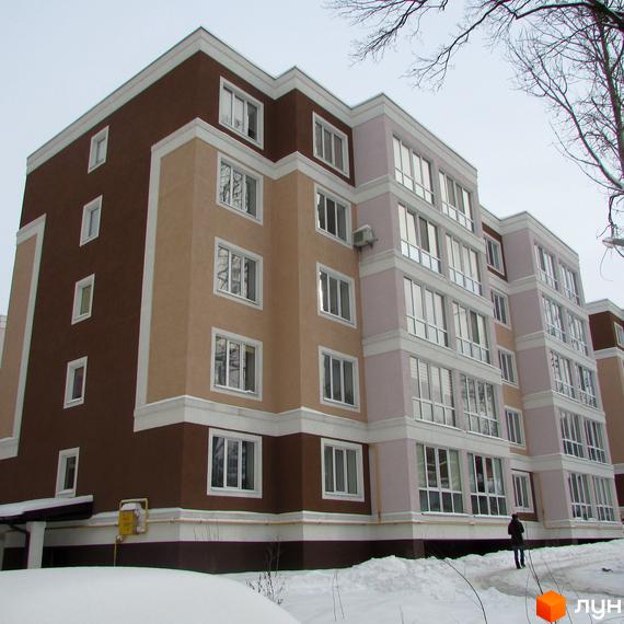 Житловий комплекс Фортуна має багатосекційну будівлю з фасадами коричневого, бежевого та світло-рожевого кольорів, прикрашеними білими елементами. Навколо будинку вкрита снігом територія з доріжкою та деревами.