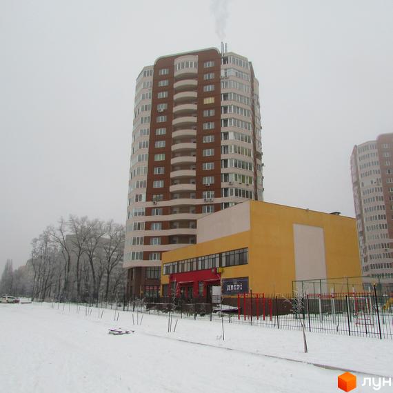 Багатоповерховий житловий комплекс Шоколад з коричневим фасадом та світлими балконами. На засніженій території видно прибудову та дерева.