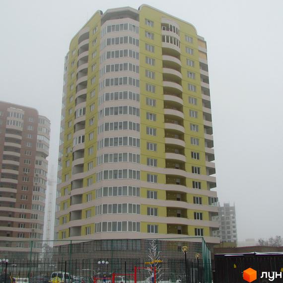 Багатоповерховий будинок житлового комплексу Шоколад світло-жовтого та бежевого кольорів з вигнутими балконами. Видно огорожу та прибудинкову територію.