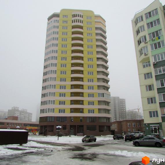 Багатоповерховий будинок Житлового комплексу Шоколад з жовто-бежевим фасадом та балконами. Прибудинкова територія вкрита снігом, видно припарковані автомобілі.