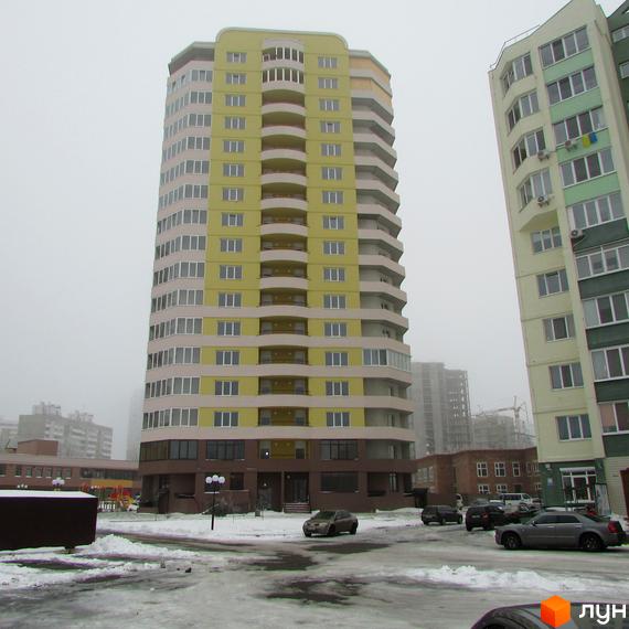 Житловий комплекс Шоколад: високий будинок жовто-бежевого кольору з балконами. Прибудинкова територія взимку з припаркованими авто та дитячим майданчиком.