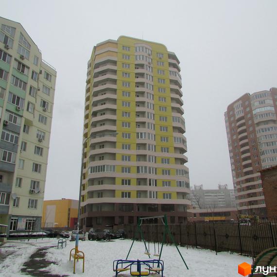 Житловий комплекс Шоколад: багатоповерховий будинок жовтого та світло-бежевого кольору з балконами. На передньому плані засніжений двір з дитячим майданчиком.