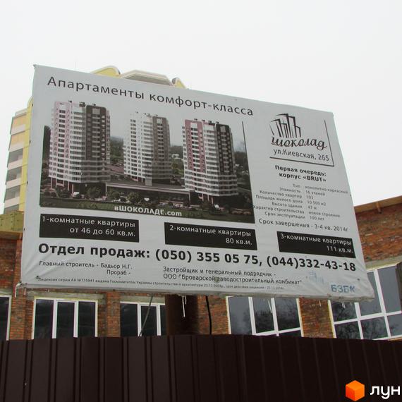 Рекламний щит Житлового комплексу Шоколад. На ньому зображено три багатоповерхові будинки світлих та темних відтінків з прилеглою зеленою зоною.