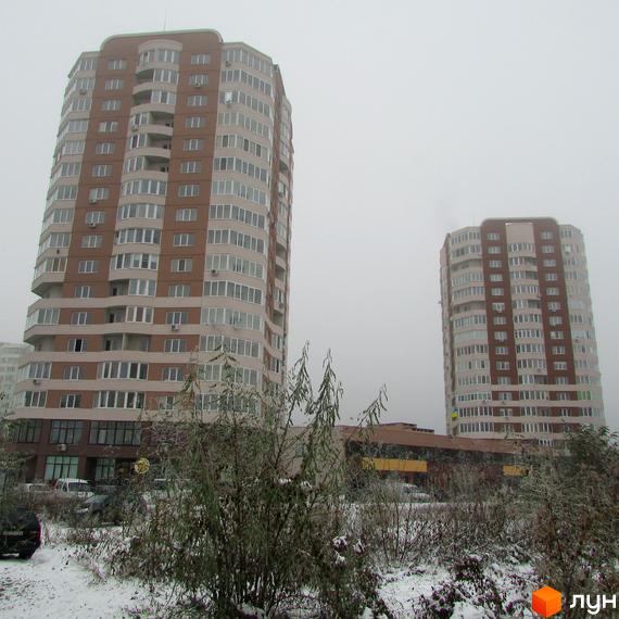 Житловий комплекс Шоколад: дві багатоповерхові будівлі з коричнево-бежевими фасадами та численними вікнами. Прибудинкова територія вкрита снігом, видно чагарники та дерева.