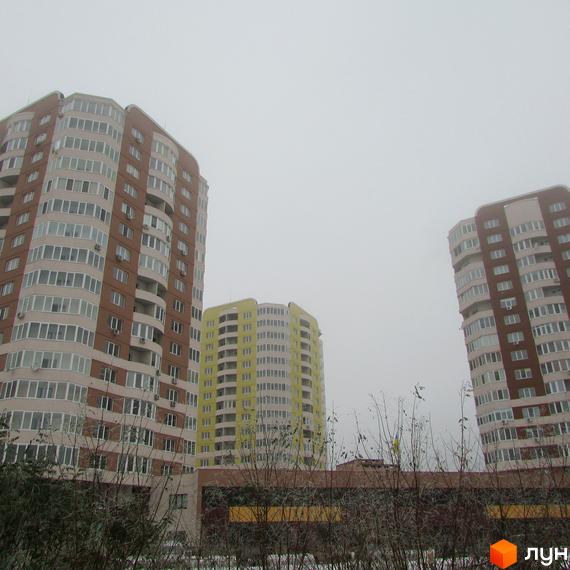 Три багатоповерхові будинки Житлового комплексу Шоколад: два коричневі та один жовтий, з багатьма вікнами та балконами. На передньому плані видно голі кущі.