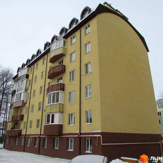 Житловий комплекс НовоОскольский має жовтий фасад, коричневу основу та дах з арковими вікнами. Будівля розташована на засніженій території з деревами.