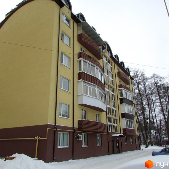 Житловий комплекс НовоОскольский: багатоповерховий будинок з жовтим фасадом, коричневим цоколем та заскленими балконами. Навколо будинку засніжена територія з деревами.
