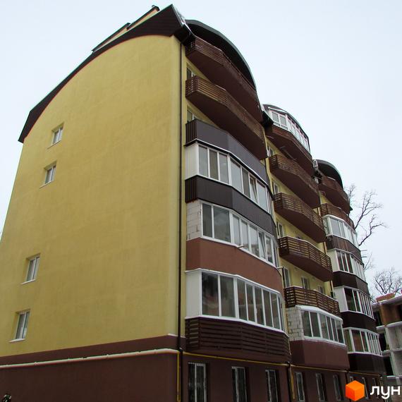 Житловий комплекс НовоОскольский: багатоповерхова будівля з вигнутим жовтим фасадом, коричневими балконами та заскленими лоджіями.