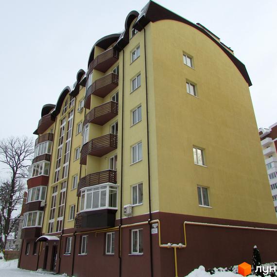 Житловий комплекс НовоОскольский: багатоповерховий будинок з жовтим фасадом, коричневою основою та балконами. Навколо засніжена територія та оголене дерево.