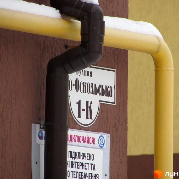 Будинок Житлового комплексу НовоОскольский з коричневим фасадом. Видно водостічну трубу, жовту газову трубу зі снігом та табличку з адресою.
