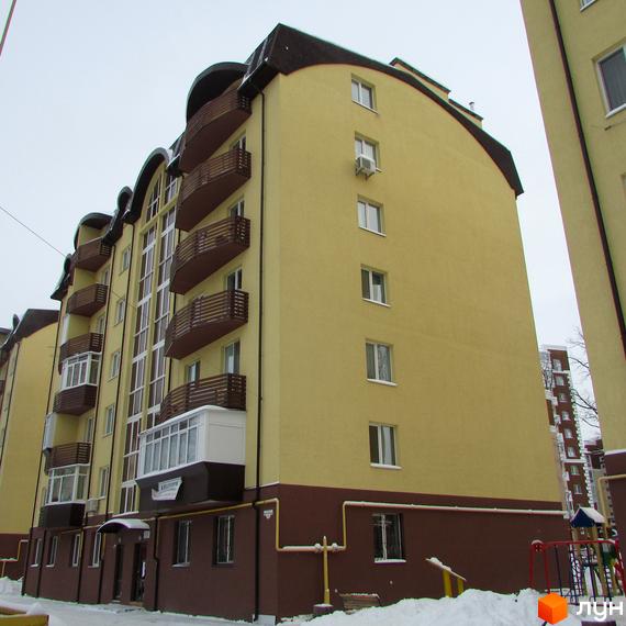 Новобудова НовоОскольский: багатоповерховий будинок з жовто-коричневими фасадами, вигнутим дахом та балконами. Навколо сніг та дитячий майданчик.