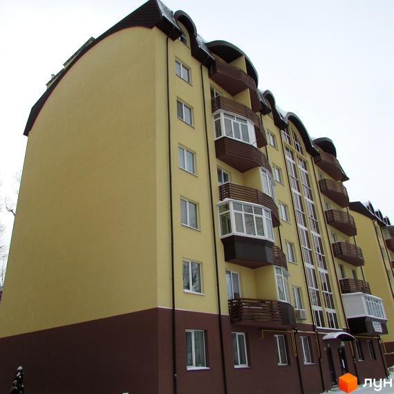 Житловий комплекс НовоОскольский: багатоповерховий будинок з жовто-коричневим фасадом, білими вікнами та вигнутим дахом. Видно балкони та сніг на ділянці.