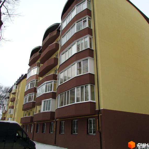 Новобудова НовоОскольский: багатоповерховий будинок з жовто-коричневим фасадом, вигнутими формами та заскленими балконами. Навколо сніг і дерева.