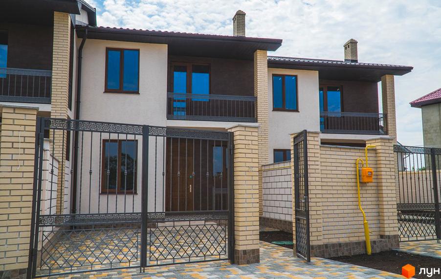 Двоповерховий будинок ж/м «Червоний Хутір» з балконами та цегляними колонами. Перед новобудовою металеві ворота та бруківка на подвір'ї.