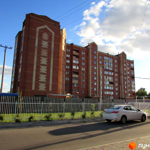 Житловий комплекс Левада – цегляна багатоповерхівка з білими декоративними елементами. Прибудинкова територія огороджена білою огорожею, перед будинком ростуть зелені кущі.