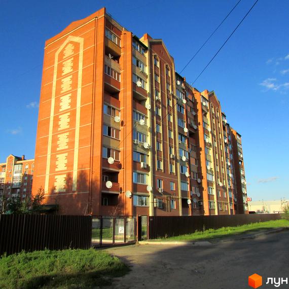 Зовнішній вигляд цегляної новобудови ЖК Левада з численними супутниковими антенами на фасаді. Територія перед будинком огороджена парканом, поруч зелена зона та дорога.