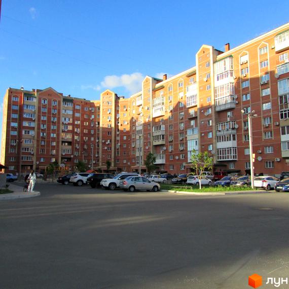 Житловий комплекс Левада. Зовнішній вигляд цегляних будинків з багатьма вікнами та балконами. Прибудинкова територія з парковкою та зеленими насадженнями.