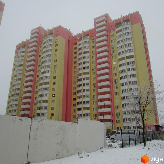 Багатоповерховий житловий комплекс на вулиці Симона Петлюри, 36, 36а, 36б. Будинок має жовто-рожевий фасад та численні балкони. На передньому плані видно бетонний паркан та засніжену територію.