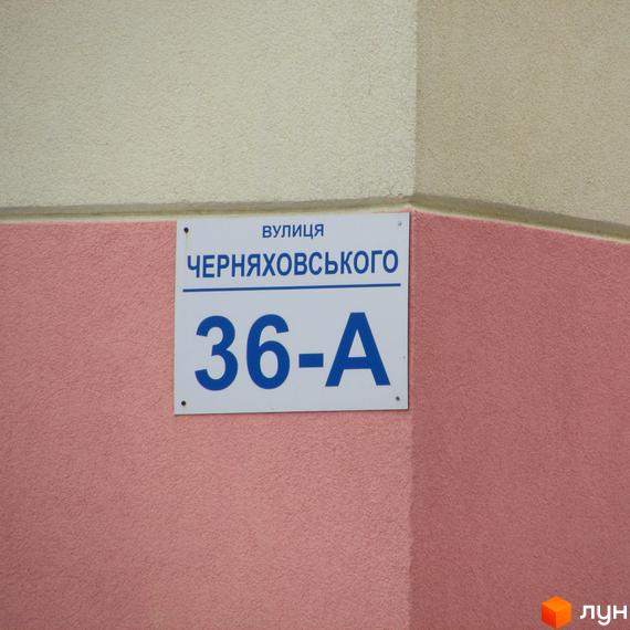 Фасад будинку вул. Черняховського, 36-А. Біла табличка з синім написом адреси будинку на рожевій стіні.