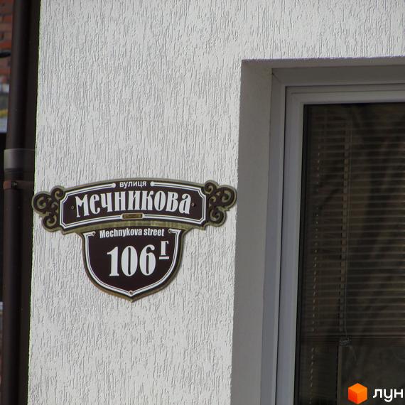 Табличка з назвою вулиці Мечникова та номером будинку 106 на білому фасаді будівлі поруч з вікном.