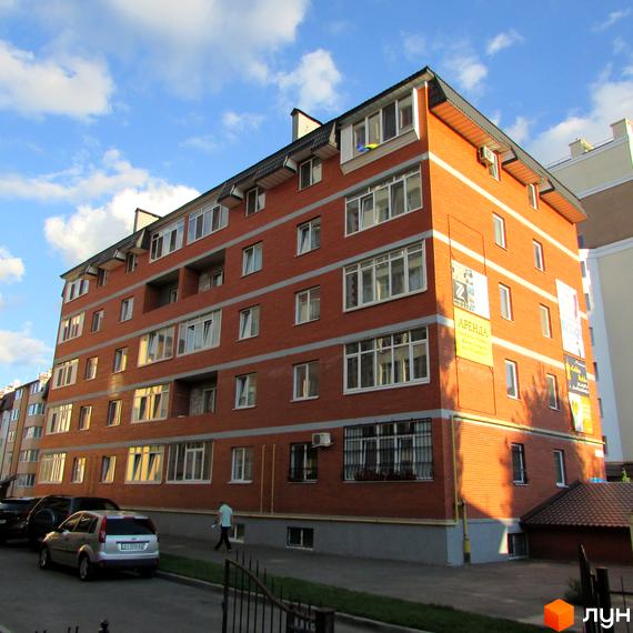 Зовнішній вигляд цегляної новобудови на вулиці Миколи Хвильового, 1. Поруч припарковані автомобілі та зелена зона.