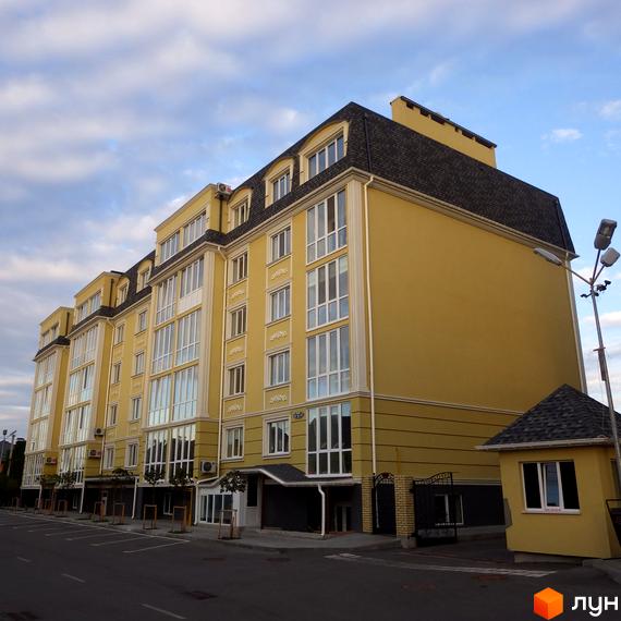 Зовнішній вигляд жовтої новобудови ЖК Софіївський пасаж з великими вікнами та темним дахом. Біля будинку розташована невелика жовта будівля охорони та освітлення.