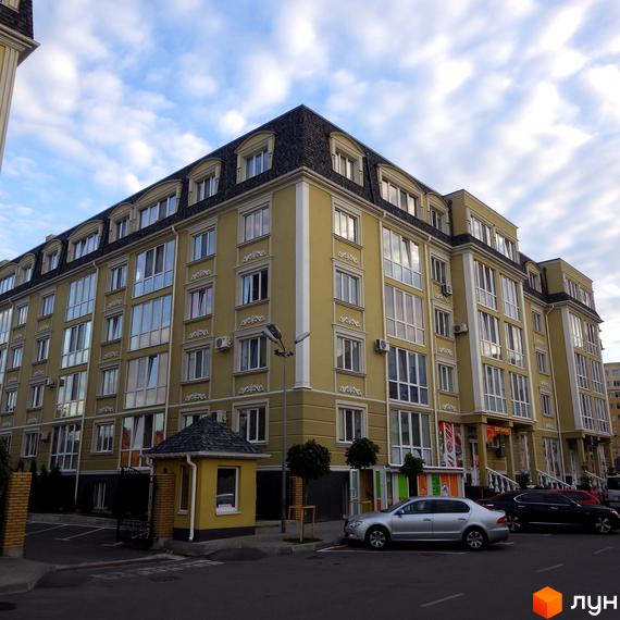 Зовнішній вигляд жовтої новобудови ЖК Софіївський пасаж з мансардними вікнами. Прибудинкова територія з парковкою та зеленими насадженнями.