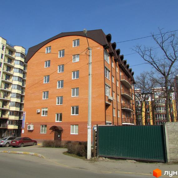 Житловий комплекс Дубовий Гай - цегляний будинок з коричневим дахом та балконами. Перед будинком розташована зелена огорожа та проїжджа частина.