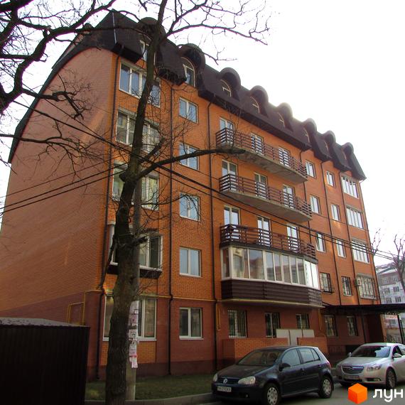 Будівельний проєкт Дубовий Гай. Цегляний будинок з балконами та мансардними вікнами. Поруч дерева та припарковані автомобілі.