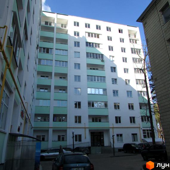 Зовнішній вигляд багатоповерхового будинку житлового комплексу Сосновий двір з балконами та вікнами. На прибудинковій території видно автомобілі та вхід до під'їзду.