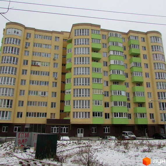 Житловий комплекс Зірка Дніпра. Багатоповерховий будинок жовтого кольору з зеленими балконами та лоджіями. Навколо будинку засніжена територія та парковка.